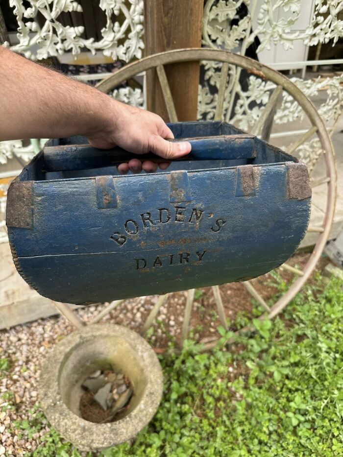 A hand holds an antique blue wooden Borden's Dairy box. An early American collectible.