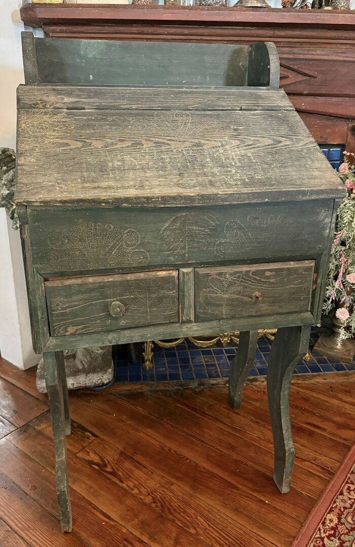 An aged, dark green antique wooden secretary desk with two drawers and carved details, a historic piece from Early America.