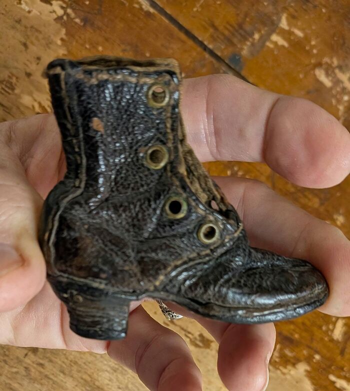 A hand holds a tiny, aged dark leather boot, a historic piece from Early America, on a wooden background.