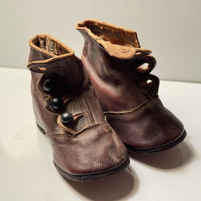 A pair of historic pieces: small, dark brown leather baby boots with black buttons, collected from Early America.