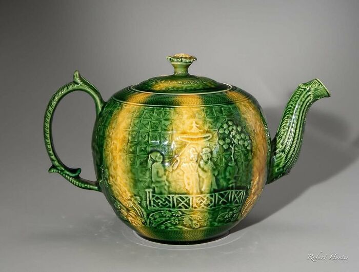 A historic piece from early America: a vibrant green and yellow ceramic teapot featuring intricate embossed figures and patterns.
