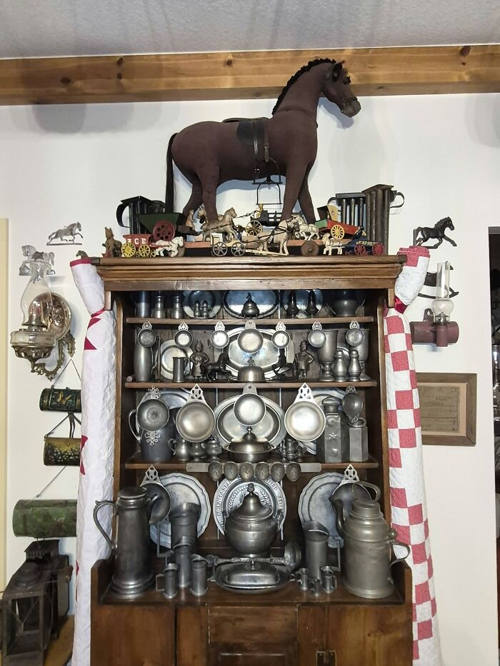 A wooden hutch filled with historic pieces from early America, including pewter dishes and miniature horse toys.