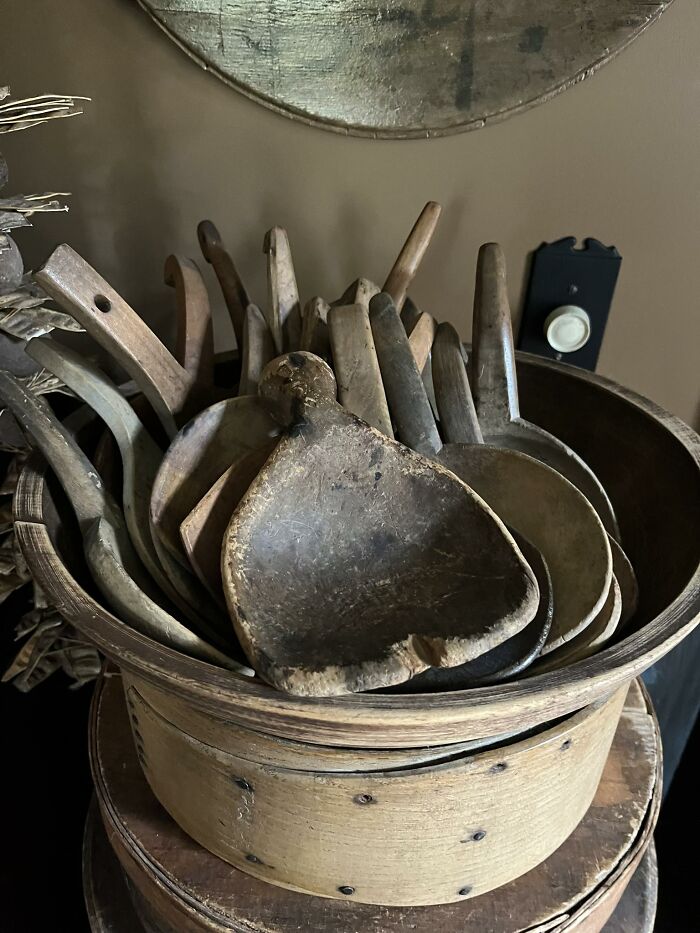 A bowl filled with various antique wooden spoons and scoops, showcasing historic pieces from early America.