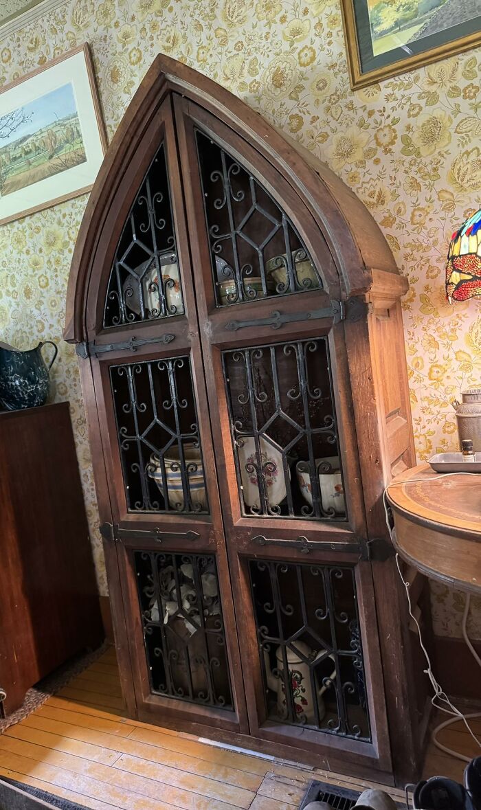 A tall, antique wooden cabinet with Gothic arches and wrought iron grilles displays historic pieces from early America.
