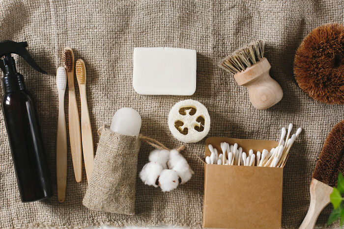 A collection of zero-waste personal care items: bamboo toothbrushes, a bar of soap, loofah, and cotton swabs. These habits can save you money.