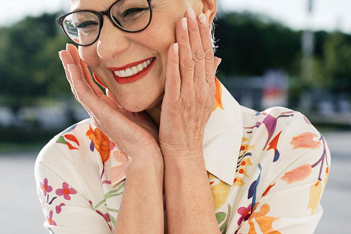 An older woman, smiling and holding her hands to her face, reveals if older people regret not having kids.