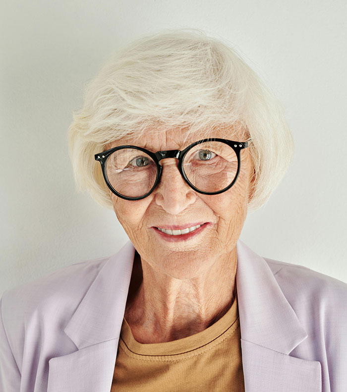 An older woman with white hair and glasses, smiling at the camera, exemplifying older people who chose not to have kids.