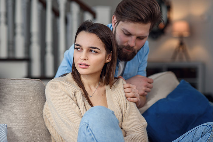Couple sitting on sofa, woman looking away looking upset in cozy home setting Couple sitting on sofa, woman looking away looking upset in cozy home setting