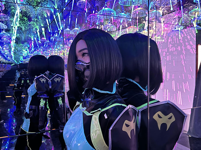 Cosplayer in futuristic costume posing in mirrored room with colorful lights Cosplayer in futuristic costume posing in mirrored room with colorful lights