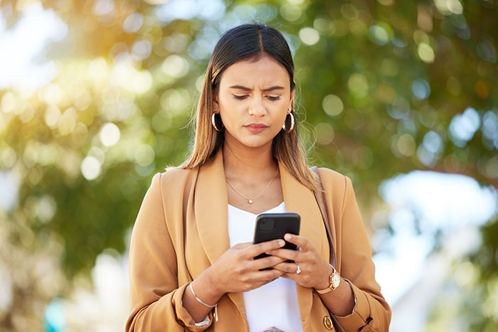 Woman looking concerned while checking her phone outdoors Woman looking concerned while checking her phone outdoors