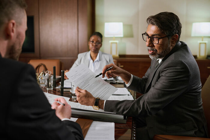 Three lawyers discussing hard cases. An older lawyer in glasses points to a document while a man signs.
