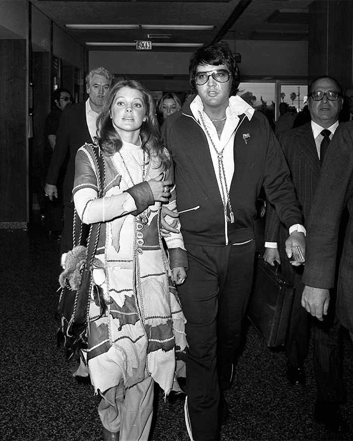 Black and white photo of Elvis and Priscilla Presley walking. Priscilla looks concerned. Disgusting Creature.