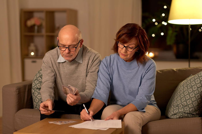 A SAHM and man managing finances, with the woman signing documents and the man counting money, dealing with debts.
