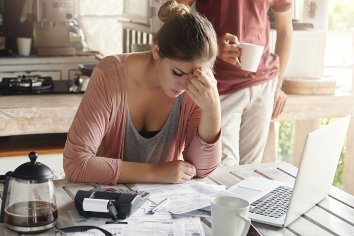 A SAHM looking distraught while reviewing bills at a table, highlighting the stress of financial burdens and debts.
