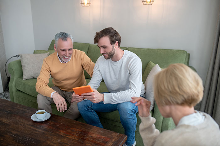 A young guy and an older man smile while looking at a tablet, potentially discussing manipulative parents.