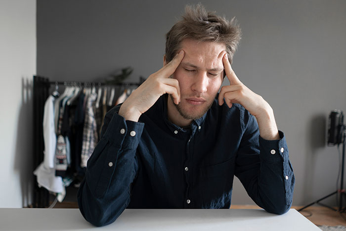 A man in a dark blue shirt, eyes closed, hands on his temples, contemplating a challenging relationship problem.