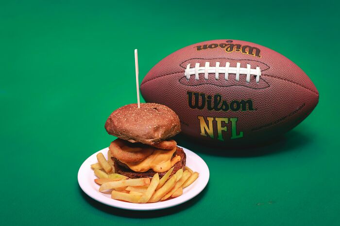 Burger and fries on a plate next to an NFL football, symbolizing Super Bowl platter controversy Burger and fries on a plate next to an NFL football, symbolizing Super Bowl platter controversy