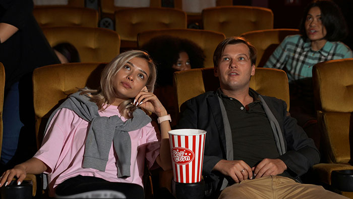 A bored woman on a first date with a man at a movie theater, she looks up with disinterest. Cringe-worthy first date.