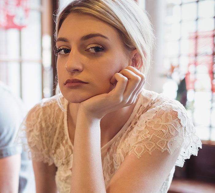 Blonde woman with a neutral expression, hand under her chin, wearing a white lace top. Cringe-worthy first date story.
