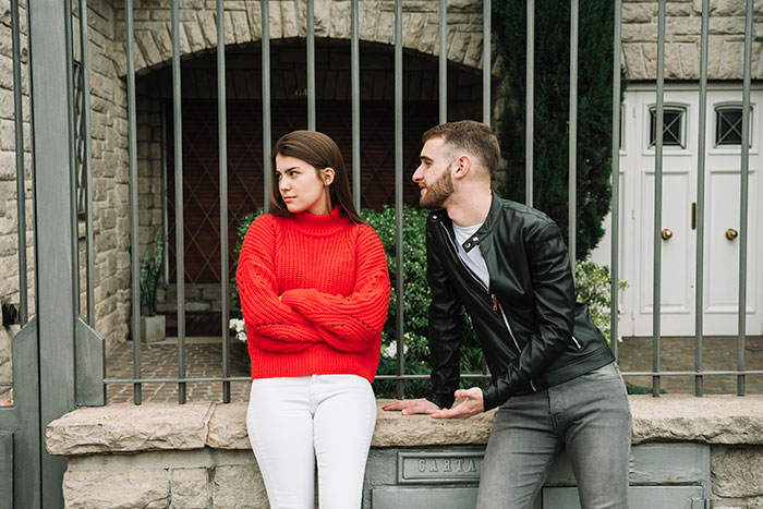 A young woman in a red sweater ignoring a man in a leather jacket, symbolizing a cringe-worthy or scary first date.