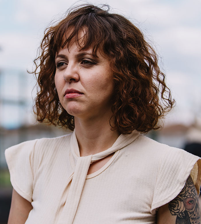 A woman with short curly brown hair and a serious expression, possibly reflecting a cringe-worthy first date story.