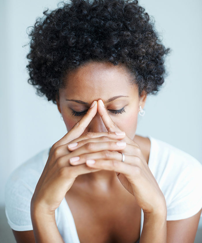 A woman with curly hair, eyes closed, fingers pressed to her forehead in distress, reflecting a cringe-worthy first date.