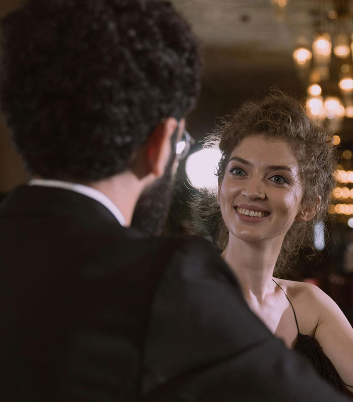 A smiling woman with curly hair looks at her date, who has his back to the camera. It’s a first date scenario.