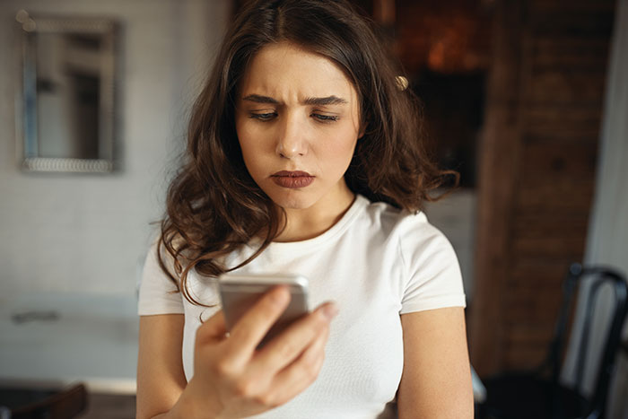 A young woman with a cringe-worthy expression looks at her phone, possibly reacting to a first date story.