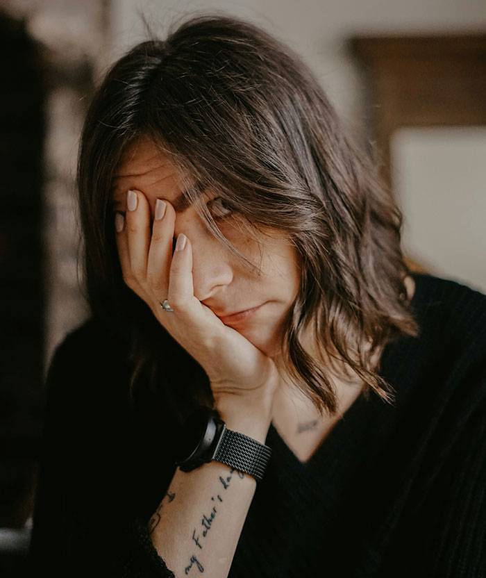 A woman with short dark hair, wearing a black shirt and a watch, resting her head on her hand, looking stressed. First date stories.