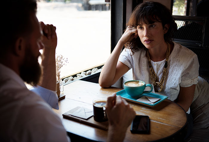 A woman with a thoughtful expression on a first date at a cafe, next to a man. Captures a cringe-worthy or scary moment.