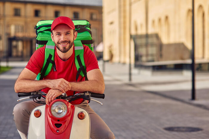 Smiling delivery man on scooter with pizza delivery backpack