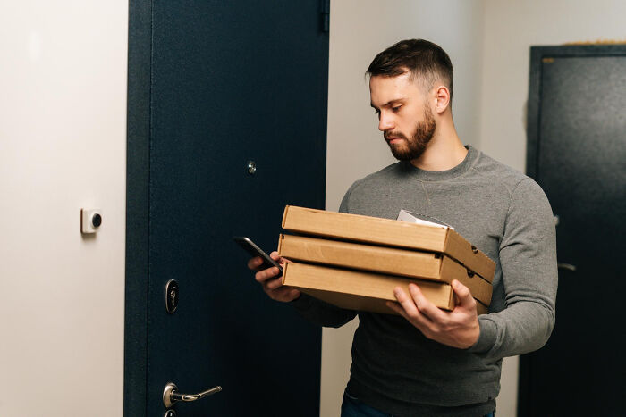 Pizza delivery driver at door holding pizza boxes checking phone