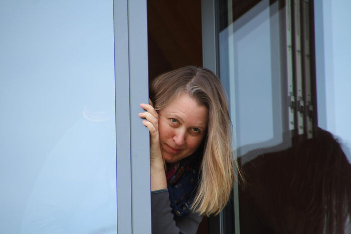 Woman peeking from behind a window frame looking outside