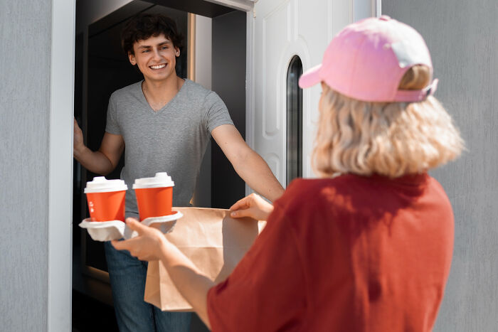 Pizza delivery person handing coffee and food bag to customer