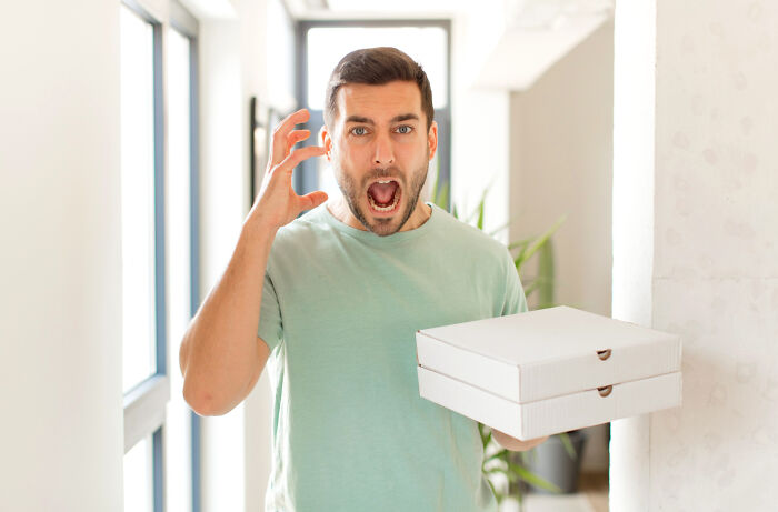 Angry man holding pizza boxes at home