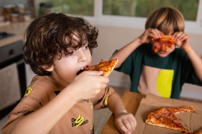 Two kids eating pizza at kitchen table