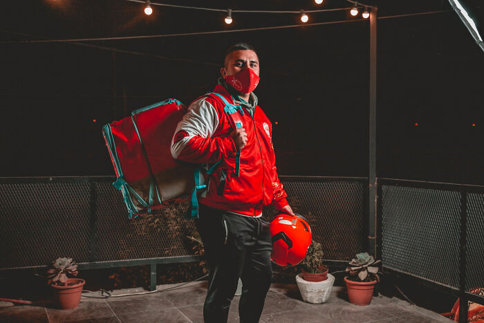 Pizza delivery person in red jacket and mask holding helmet