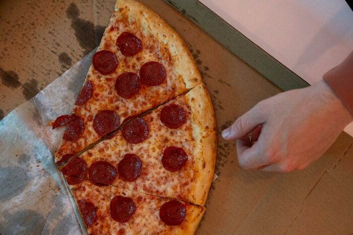 Hand reaching for pepperoni pizza slice in box