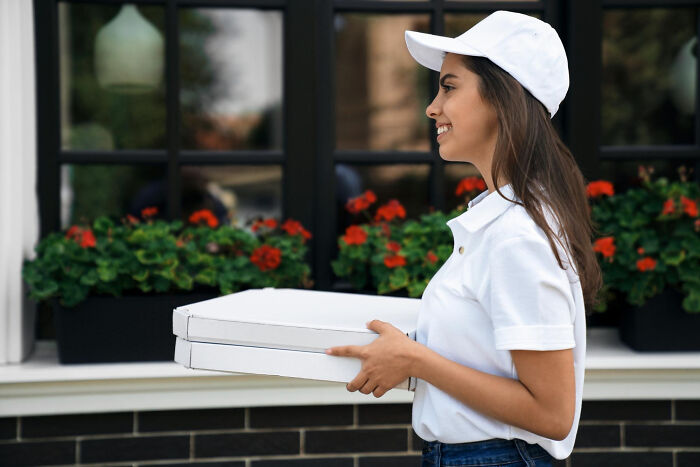 Female pizza delivery worker holding pizza boxes smiling outdoors