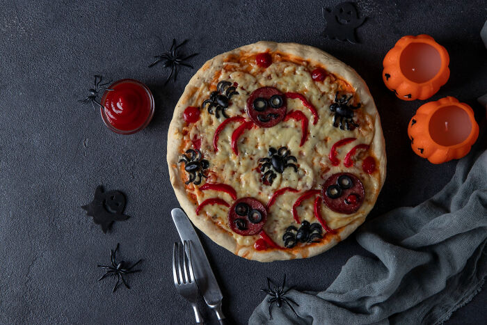 Halloween themed pizza with olives and peppers shaped like spiders on dark surface
