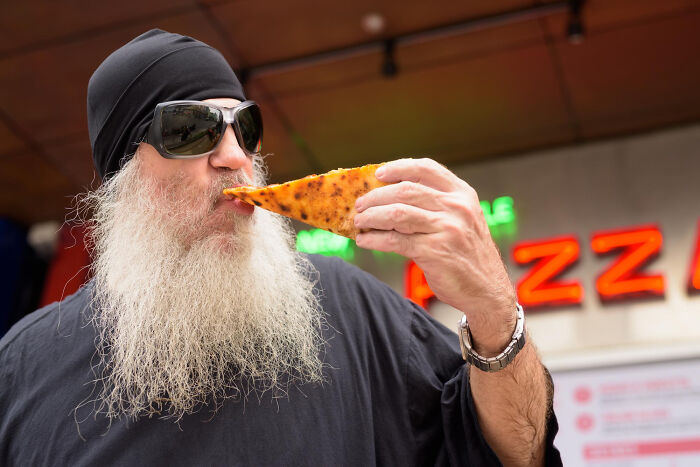 Man eating pizza slice near neon pizza shop sign