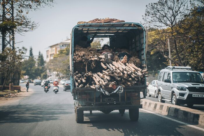 Truck carrying logs on a busy urban road with traffic around