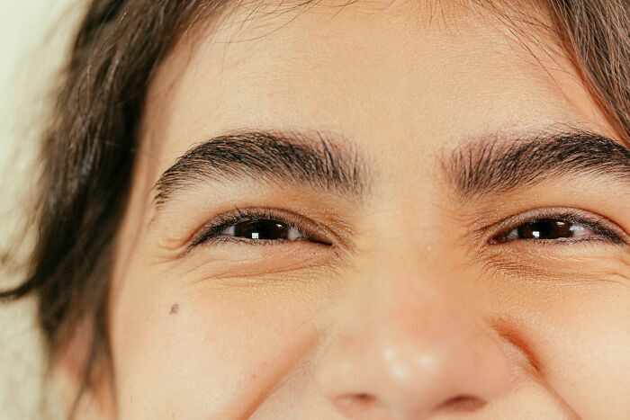Close-up of a person's eyes, eyebrows, and cheek with a mole. Their eyes crinkle, suggesting a smile. Scientific facts.
