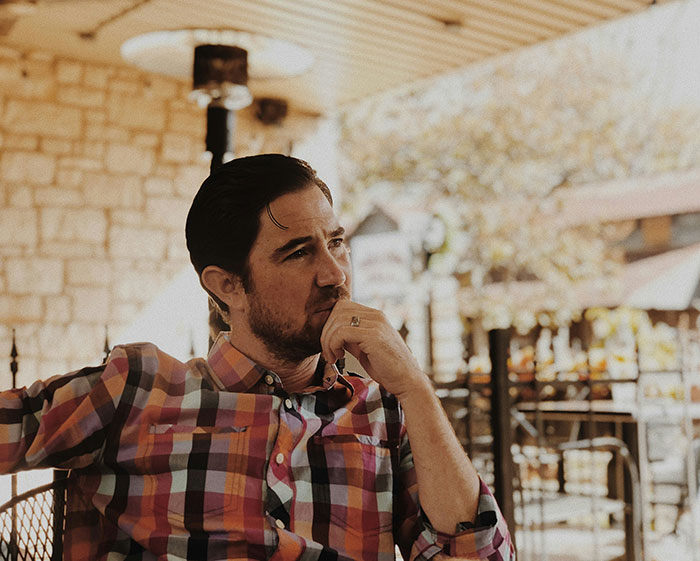 Man sitting thoughtfully outdoors in casual checkered shirt Man sitting thoughtfully outdoors in casual checkered shirt