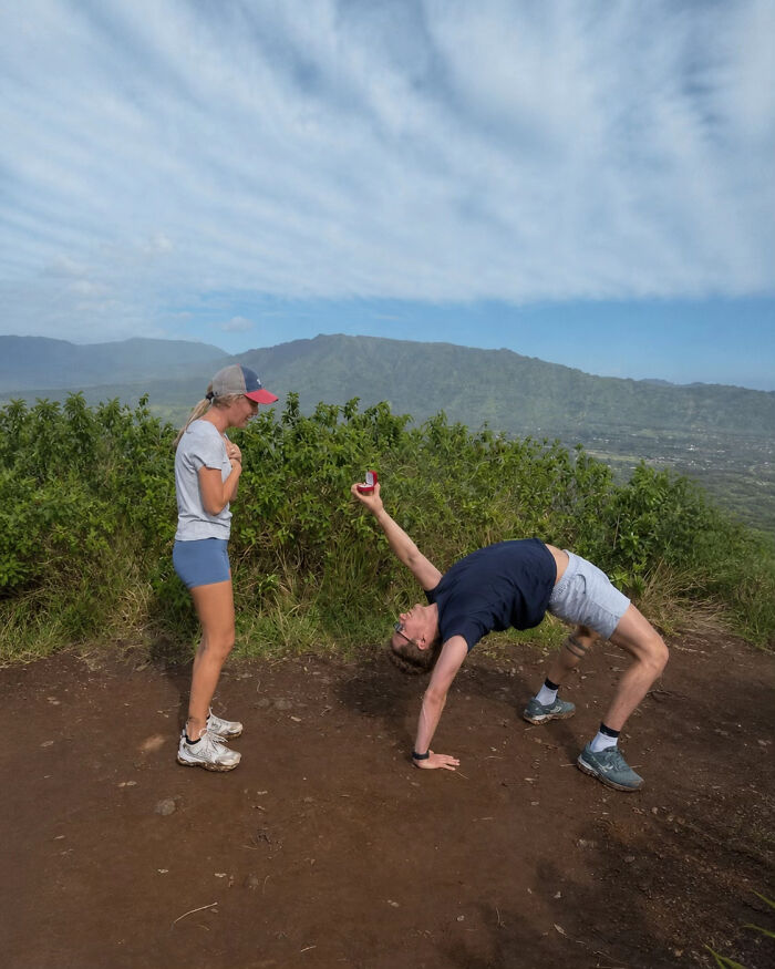 A man in a bridge pose proposes with a ring box to a woman on a mountain top, inspiring hilarious edits of the proposal pic.