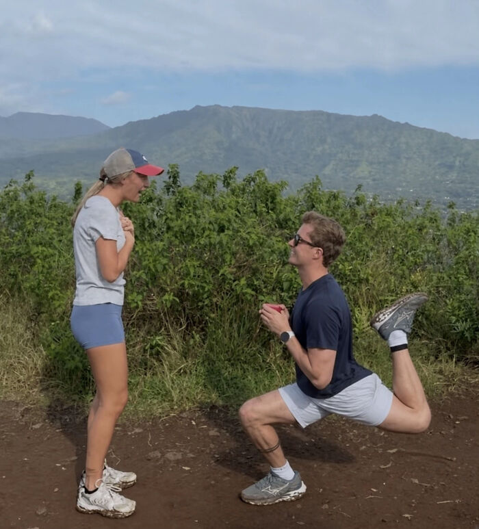 A man proposes on one knee to a surprised woman on a mountain path. This viral proposal pic inspired many edits.