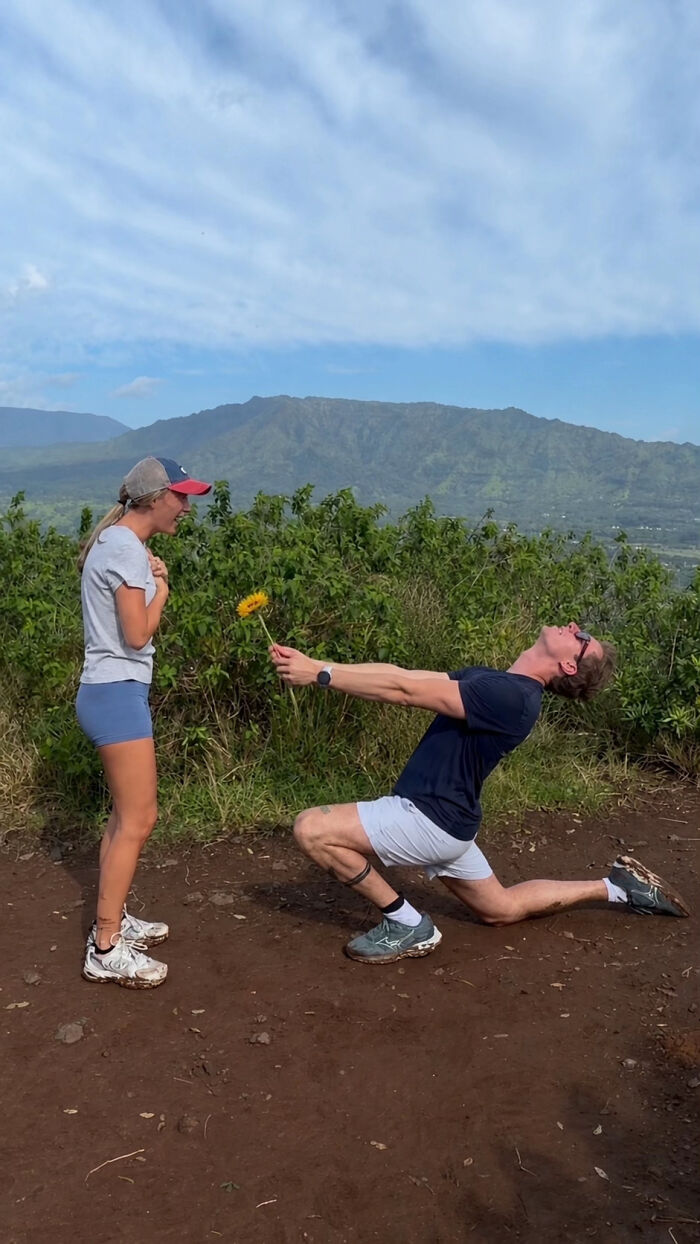Man on one knee offering a flower to a woman on a mountain top. This viral proposal pic inspired many hilarious edits.