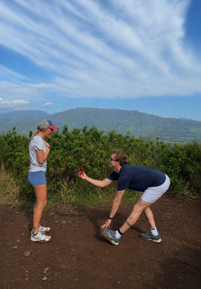 Man on one knee proposing to a woman outdoors with mountains in the background. Hilarious proposal pic edits.