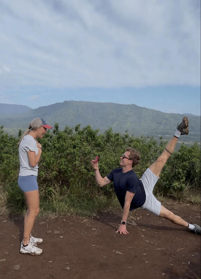 A woman reacts to a man proposing with an acrobatic pose on a dirt path overlooking mountains. This proposal pic inspired hilarious edits.