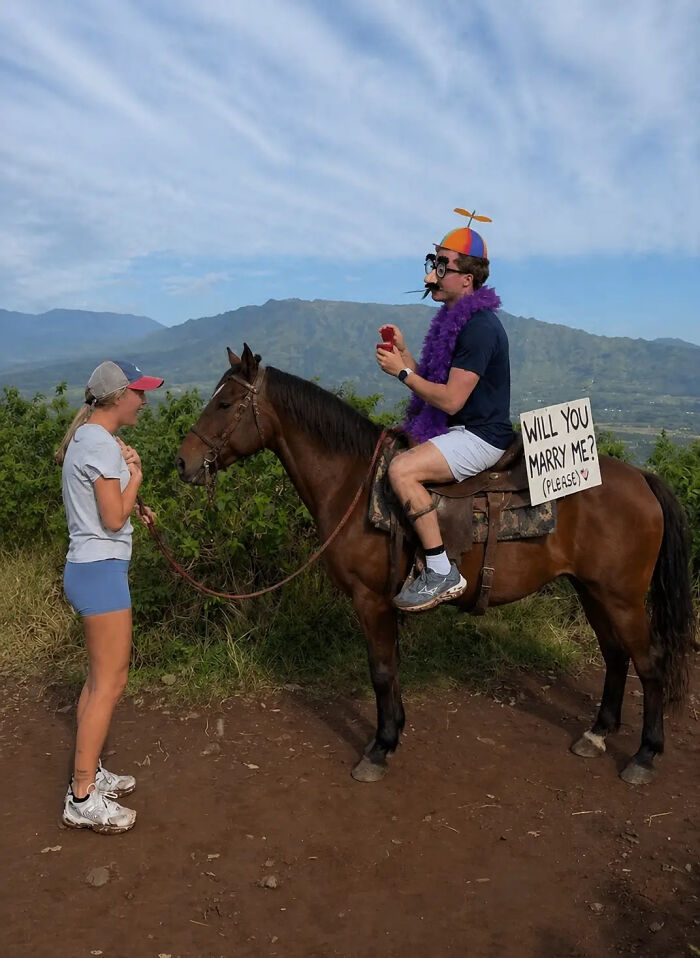 Woman's proposal pic with a man on a horse in a funny costume. Man holds a ring box and sign asking to marry.